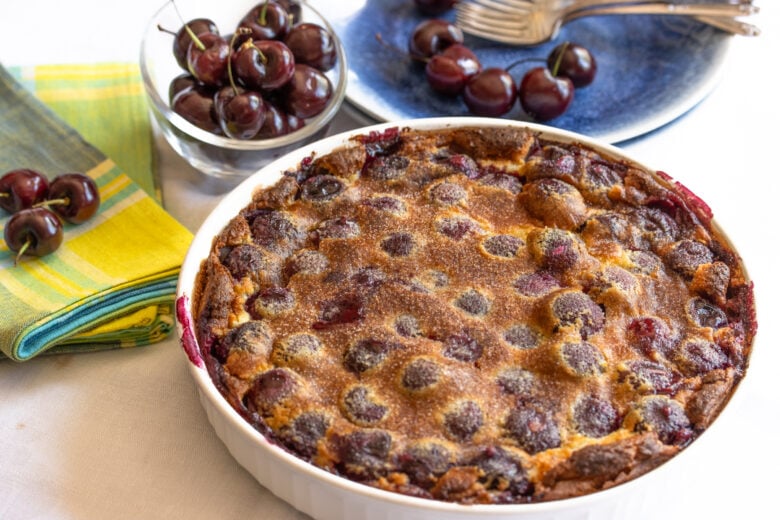 cherry clafoutis in a white baking dish surrounded by cherries