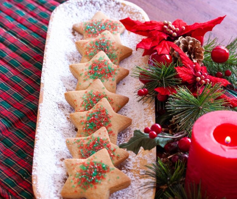 Brown sugar cookies on a white plate with Christmas poinsetta decorations and a red lite candle