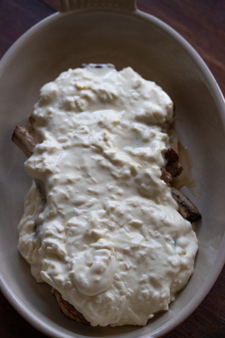 bone in pork chops with cheese spread over them ready to go under the broiler