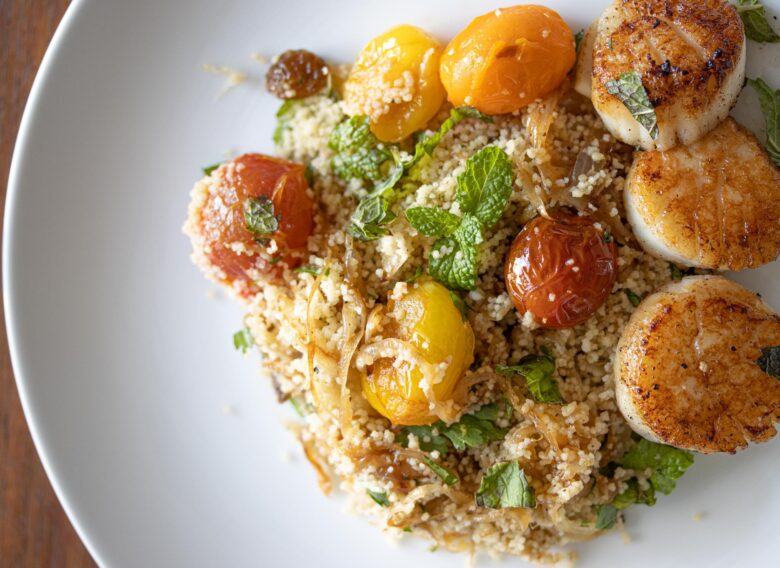 couscous salad with seared scallops on a white plate