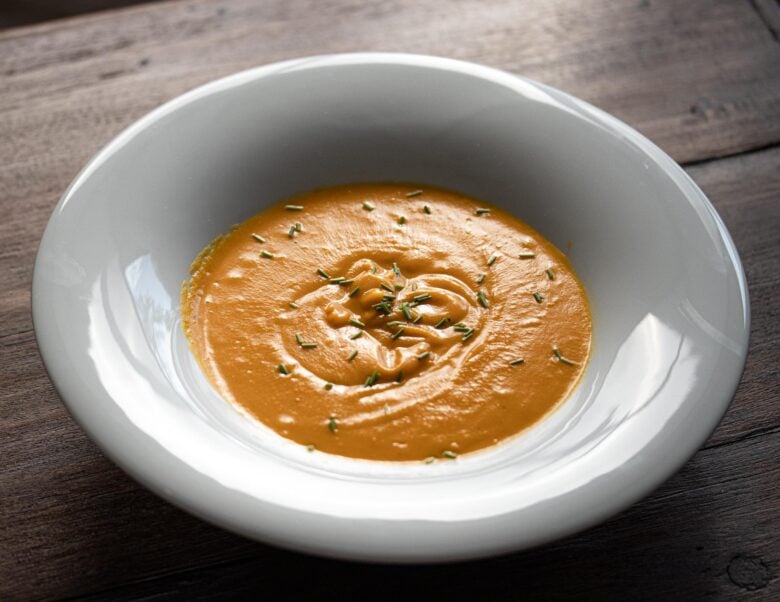 carrot soup in a white dish ona wooden table