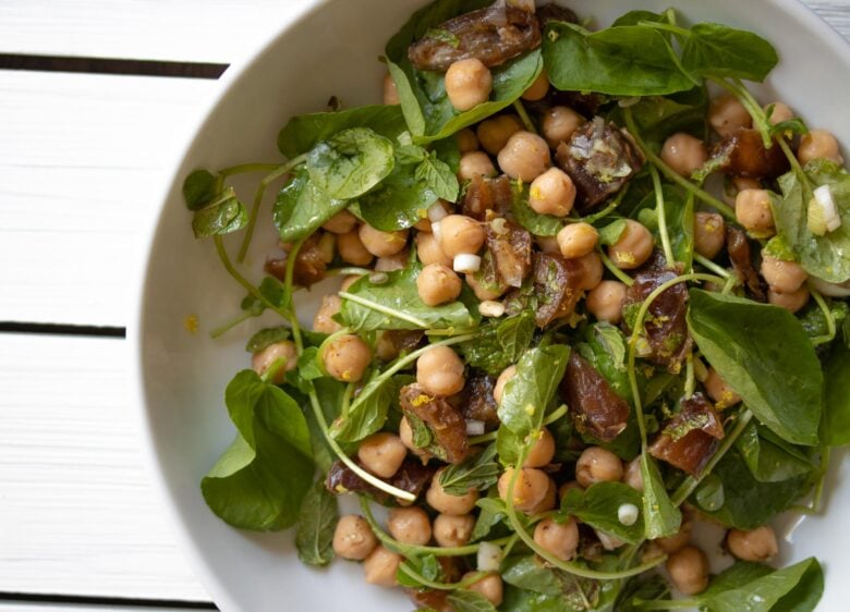 savory cresson, garbanzo beans, dates salad in a plate over a white table