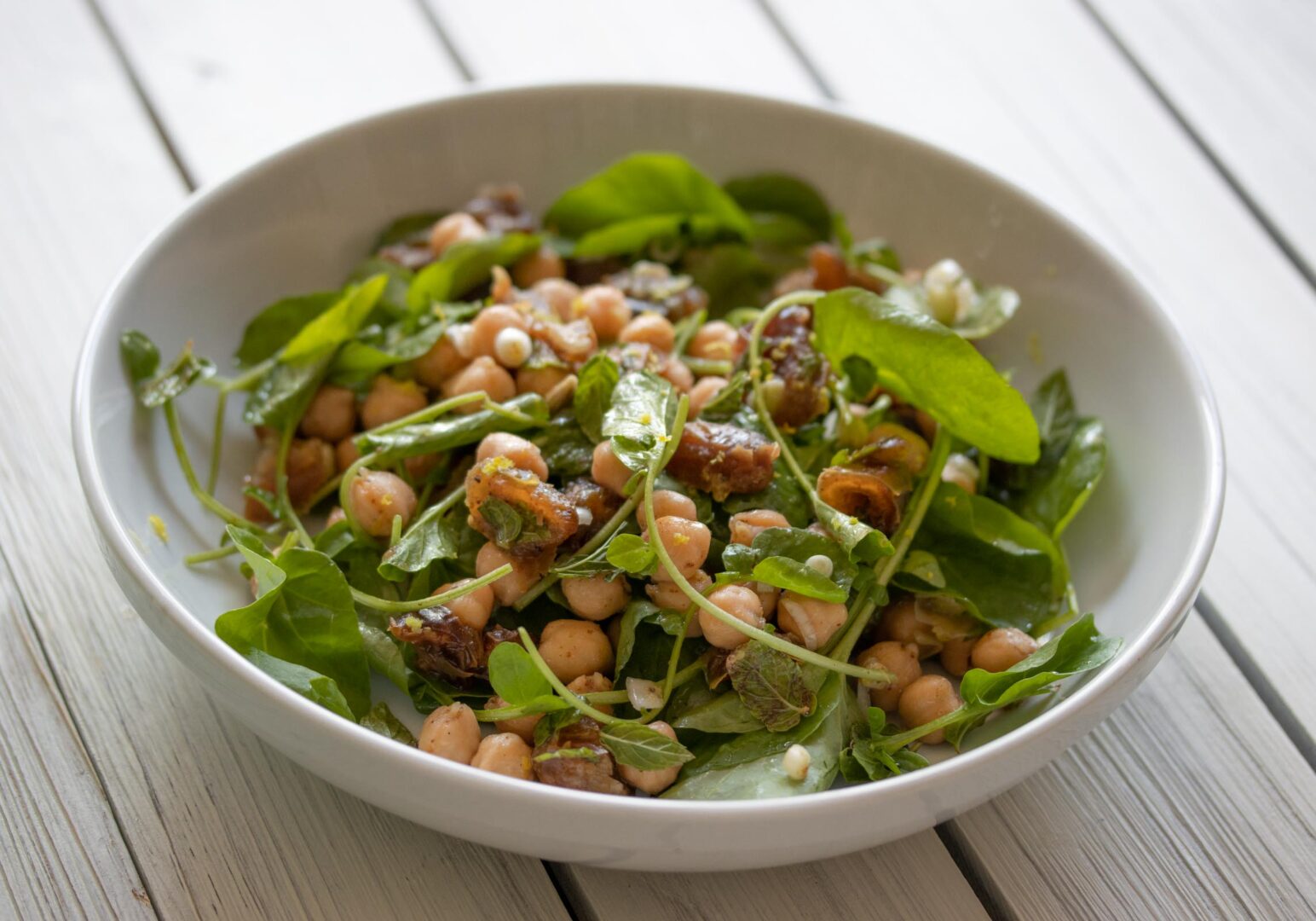 served cresson, garbanzo beans, dates salad in a white plate