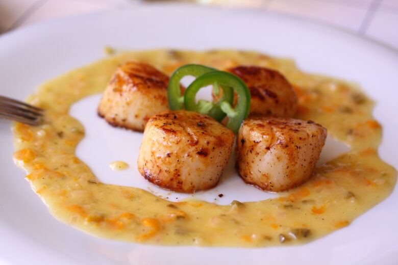 scallops on a serving plate surrounded by orange glaze sauce