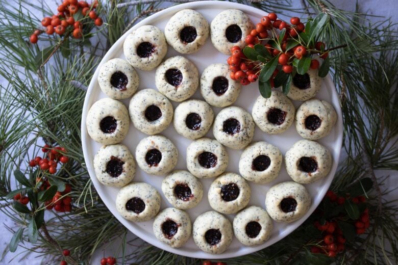 poppy seed thumbrint cookies in a plate surrounded by holiday holly 