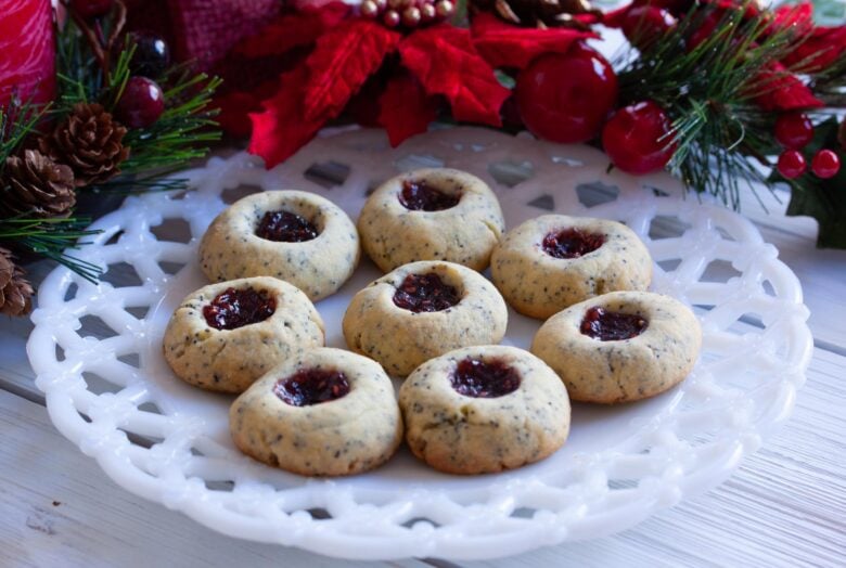 poppy see thumbprint cookies on a white plate with poinsettas flowers around it