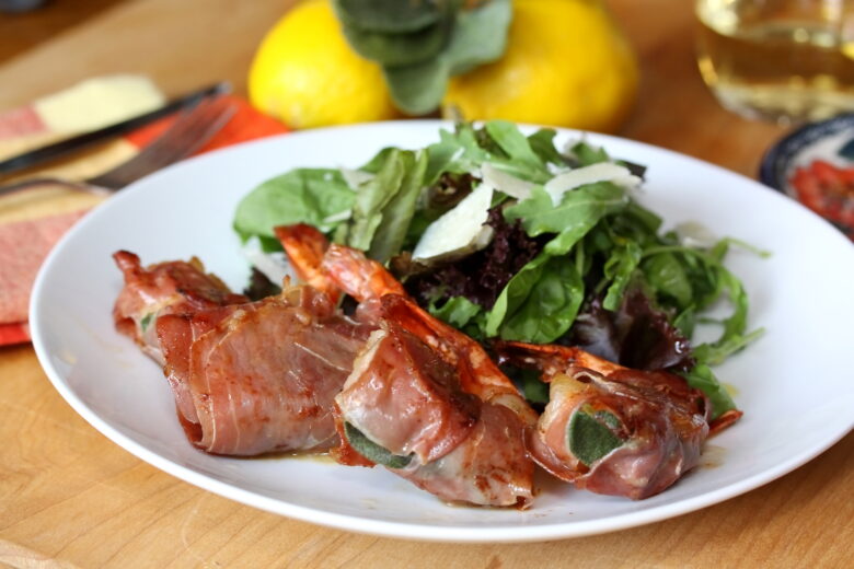 Prawns Saltimbocca on a white plate with green salad