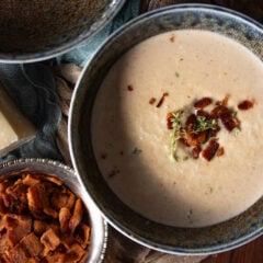 Roasted Cauliflower Soup in a blue bowl with bacon bits and parmesan cheese next to it