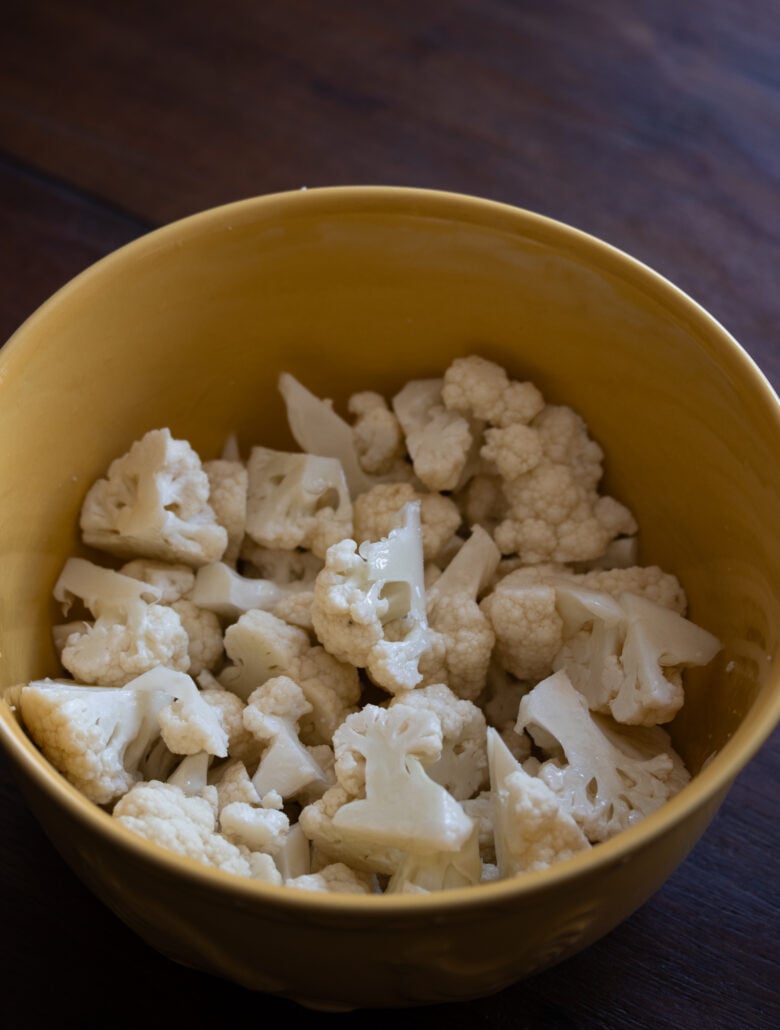 cauliflower florets in a yellow bowl mixed with olive oil