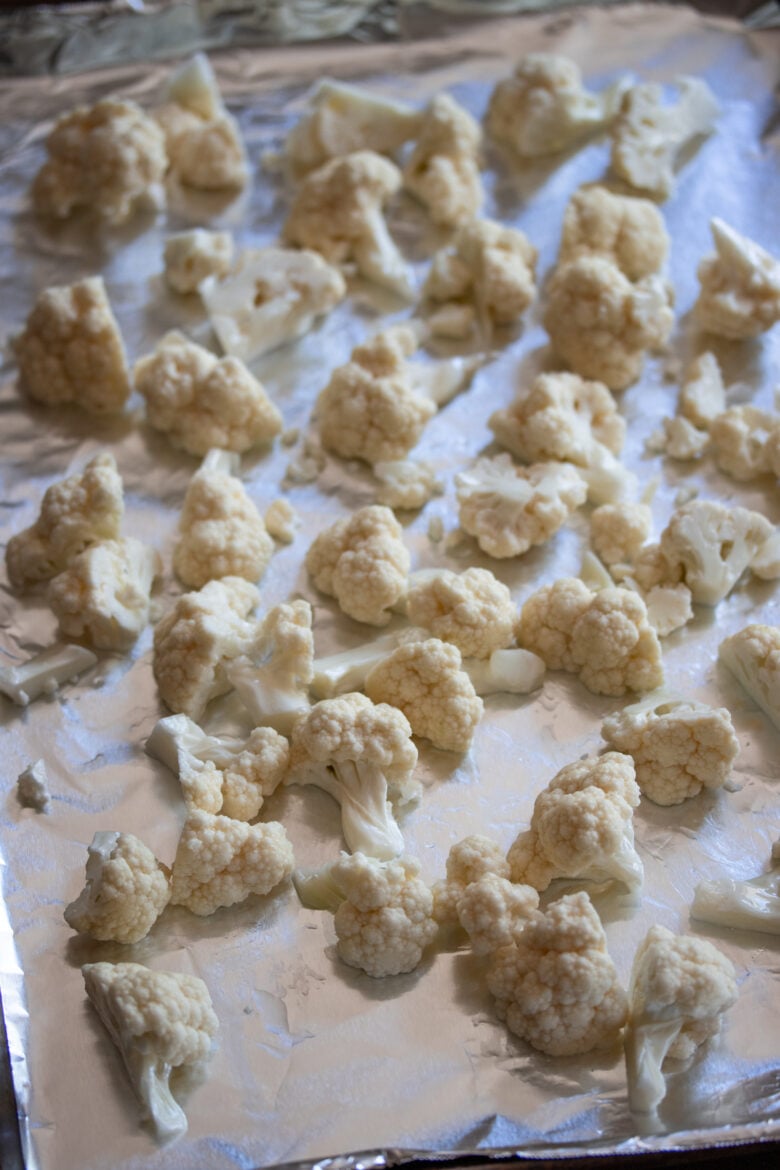 cauliflower florets laying on a cookie sheet ready to go in the oven