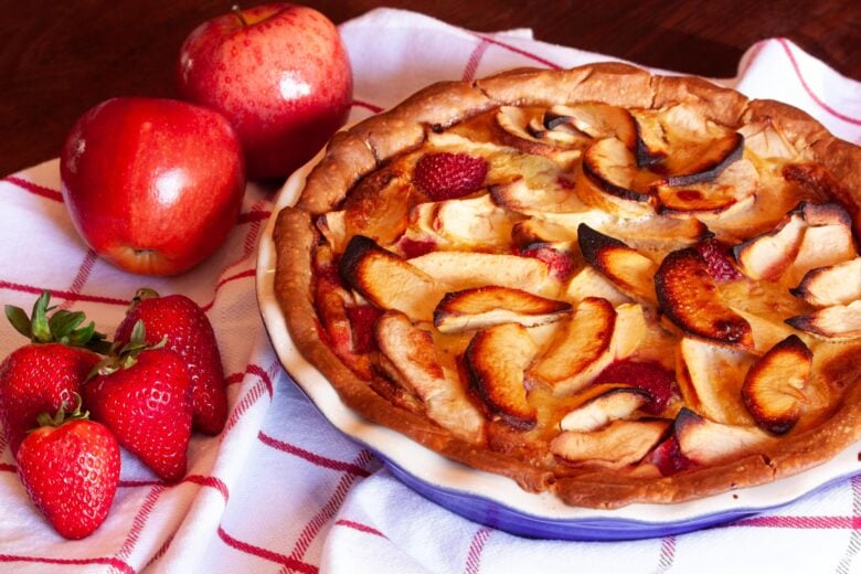 strawberry apple pie in a pie dish with apples and strawberries around it