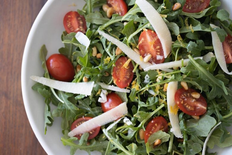 tomato arugula salad in a white serving bowl