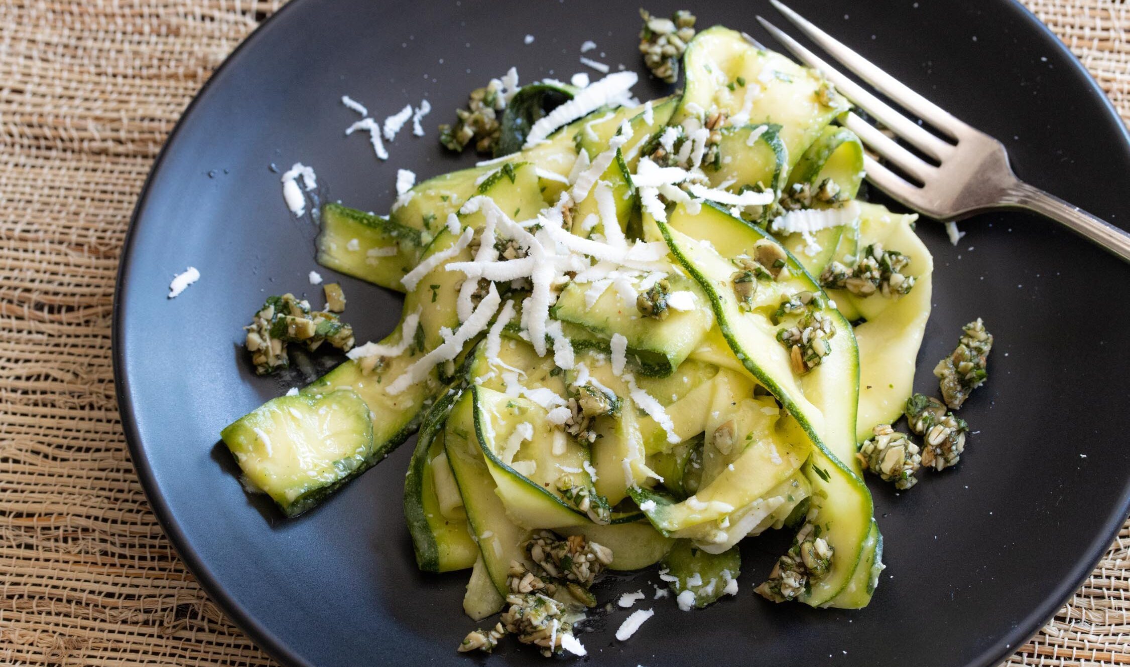 zucchini salad with avocado, pepita parsley gremolata in a black serving plate